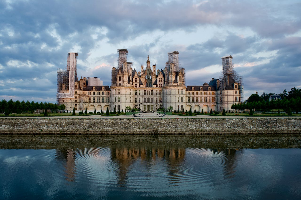 Stunning view of Château de Chambord with its reflection in serene water, under a dramatic sky.